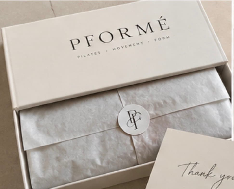 A PFORMÉ box, lid printed with the wordmark, opened to reveal tissue paper sealed with the PF monogram sticker and a handwritten thank-you card.